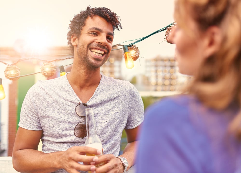 Multi-ethnic millenial couple flirting while having a drink on rooftop terrasse at sunset-2